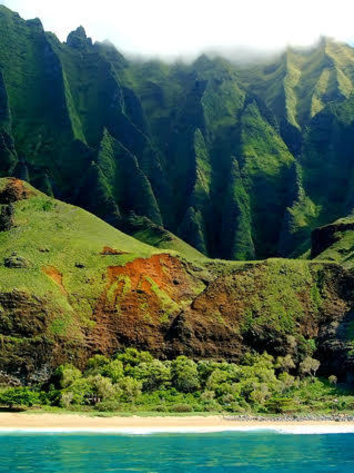 Lush green cliffs with a sandy beach and turquoise water in the foreground.