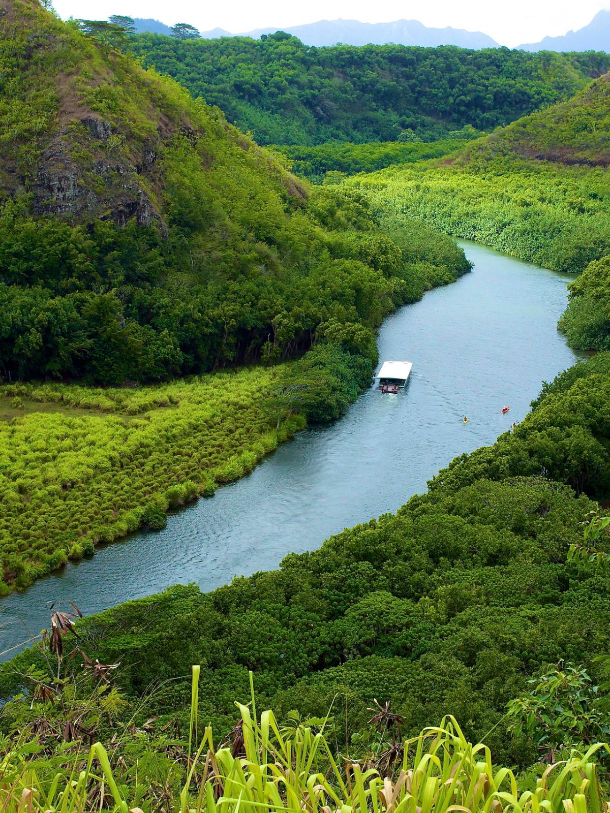River winding through lush green hills with a small boat on the water.