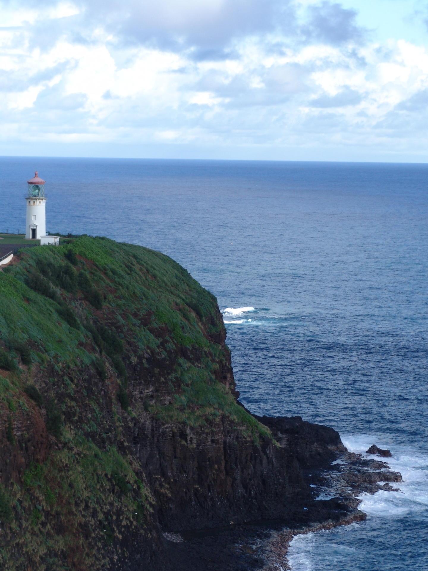 Lighthouse on a grassy cliff overlooking the ocean under a cloudy sky.